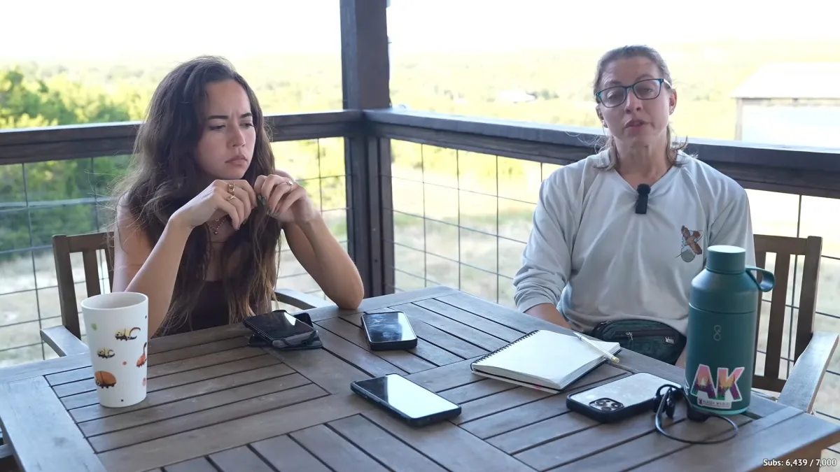 Two women sit at an outdoor table with phones.
