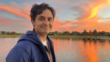 Man smiling by lake with sunset sky.