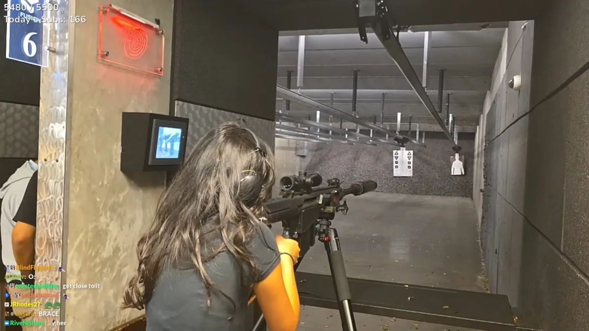 Woman aims scoped rifle at targets in indoor shooting range