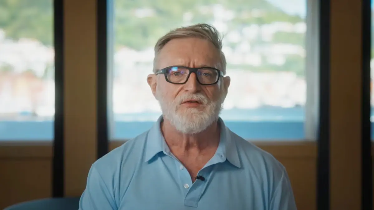 Bearded man wearing glasses speaks indoors before a window