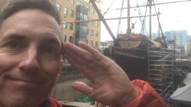 Person saluting near an old sailing ship docked.