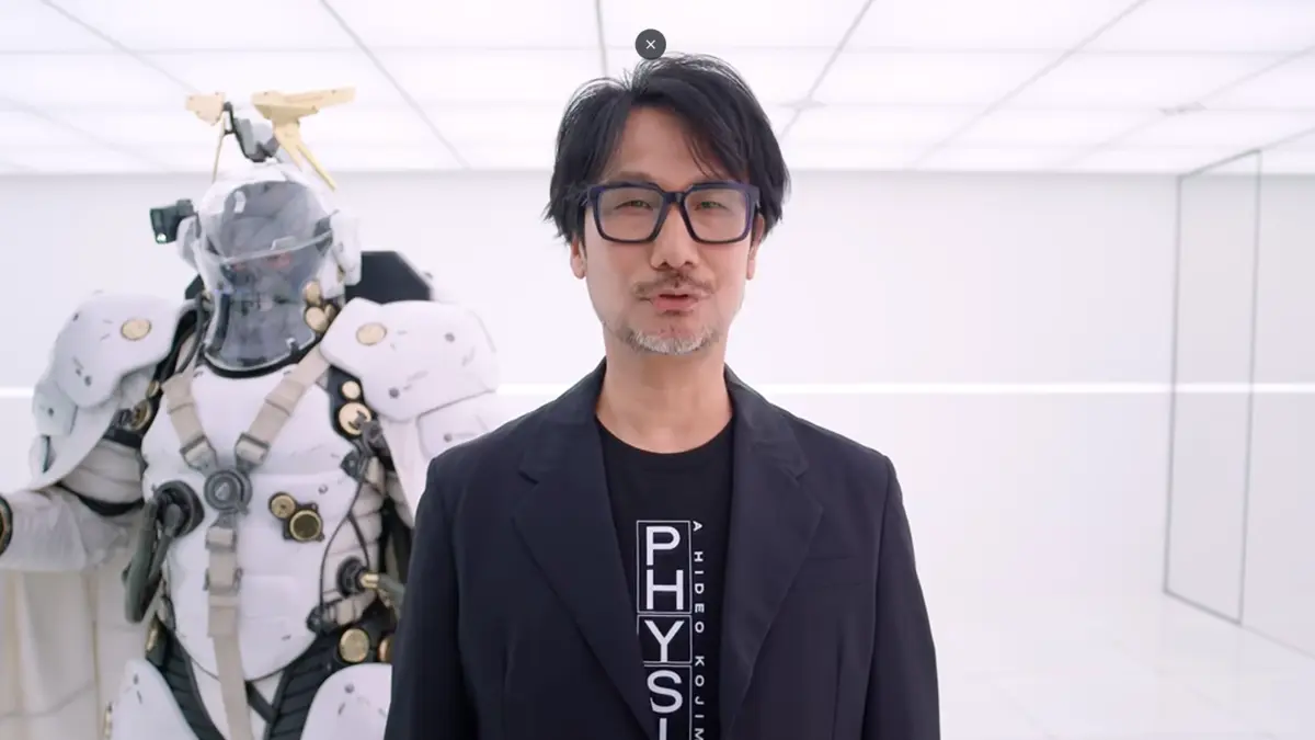 Hideo Kojima stands beside futuristic white armored robot