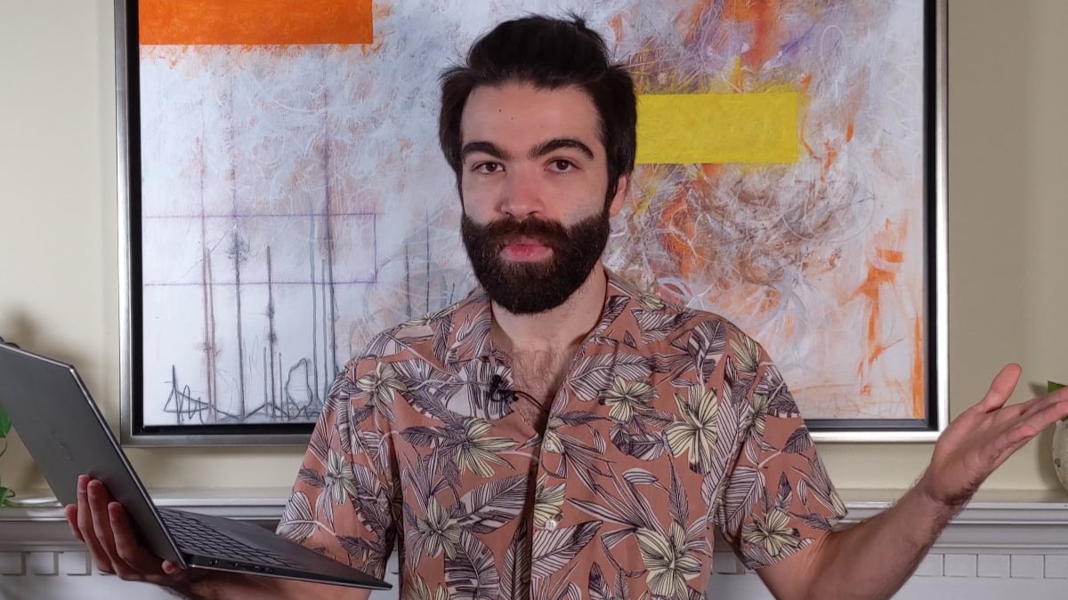 Man holding laptop gestures before abstract painting