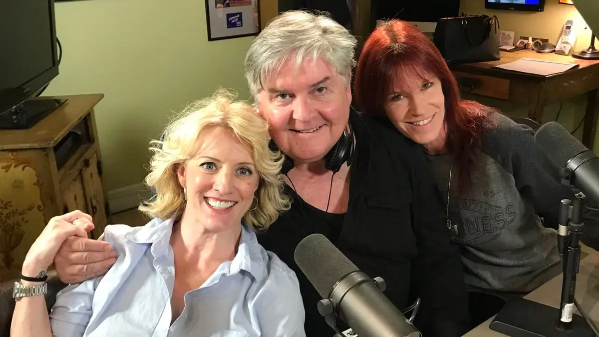 Three people smiling behind studio microphones