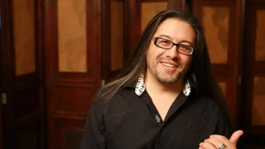 Smiling person with long hair and glasses indoors