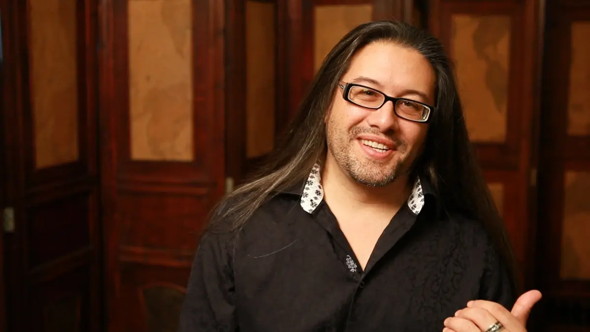 Smiling person with long hair and glasses indoors