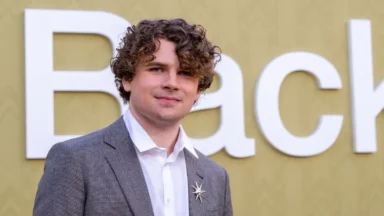 Curly-haired man in gray suit before Back sign