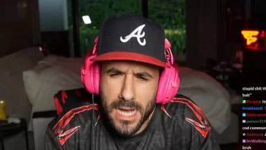 Person streaming with pink headphones and baseball cap.