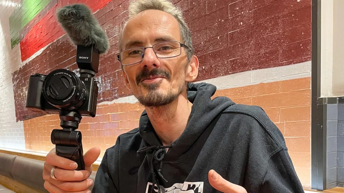 Person holding a camera indoors, smiling.