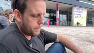 Man sitting outside convention center near TwitchCon sign