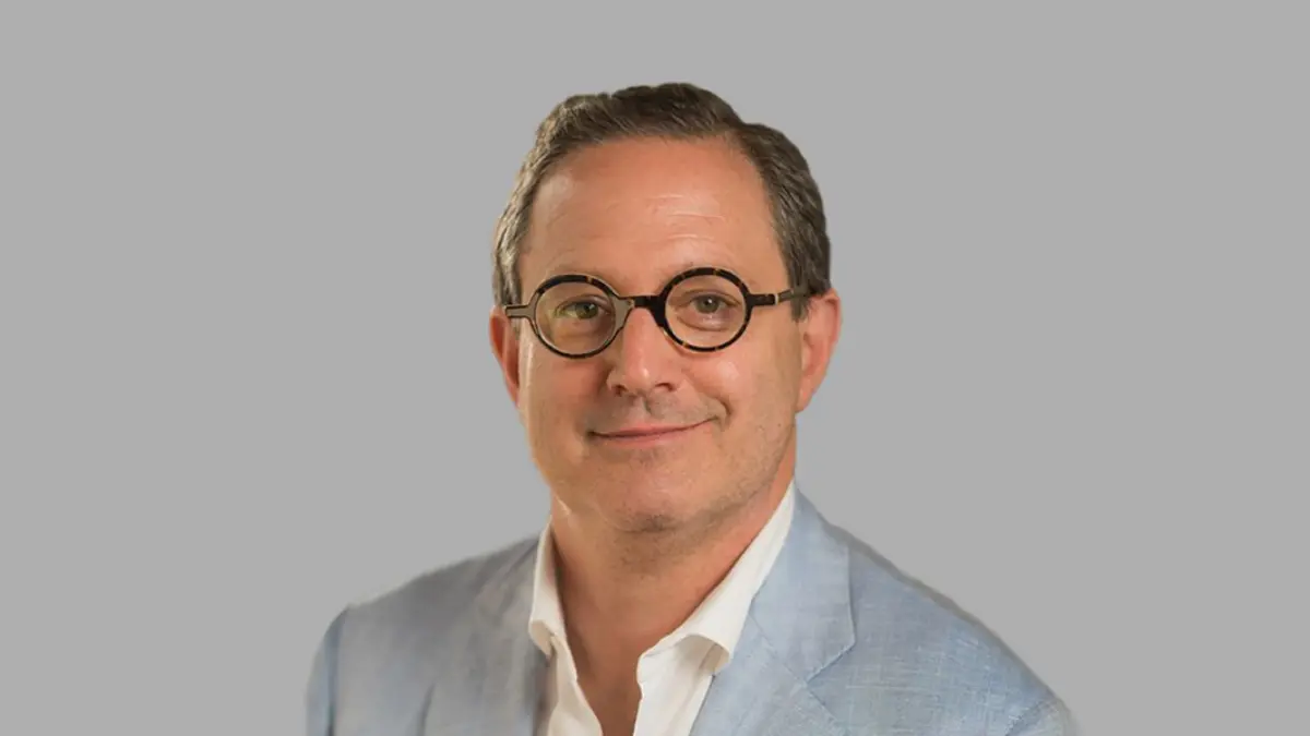 Smiling man wearing glasses and light blue blazer