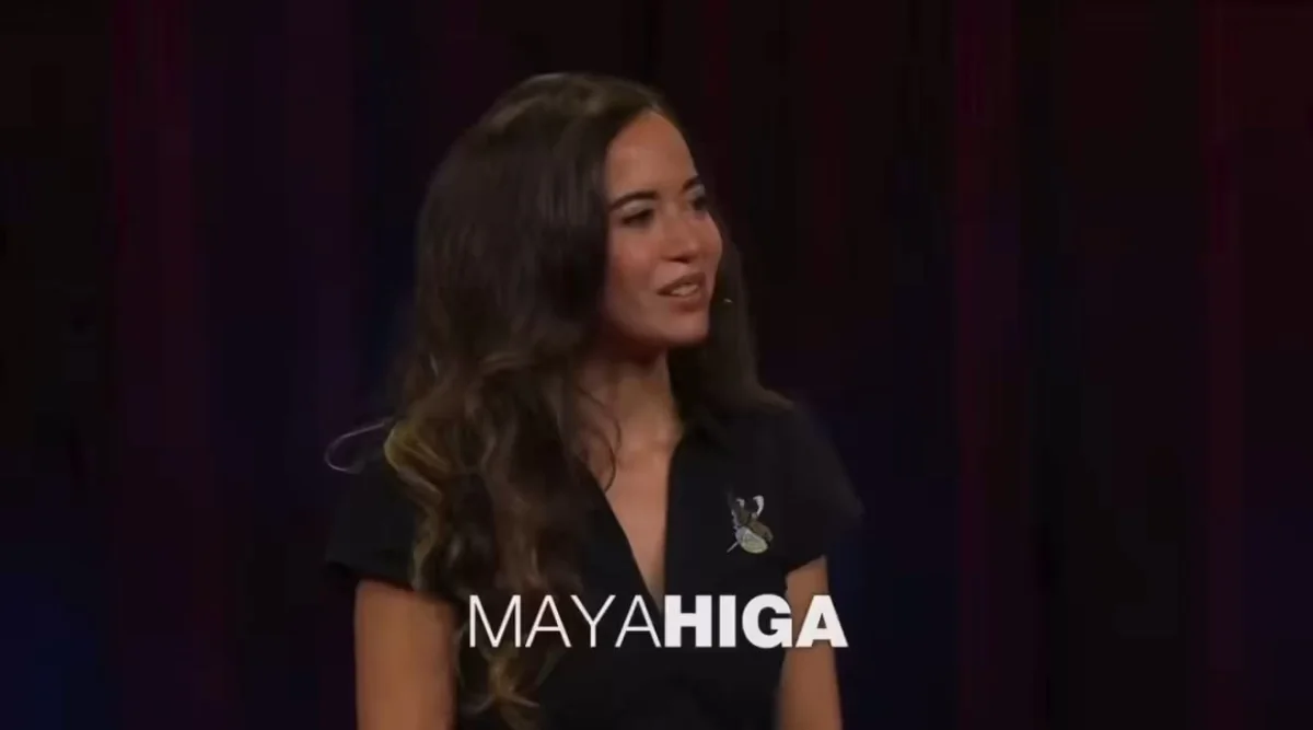 Woman speaking on stage with 'MAYA HIGA' text