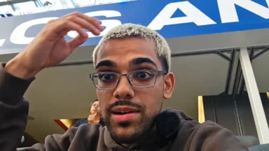 Man with glasses gestures beneath a large blue sign