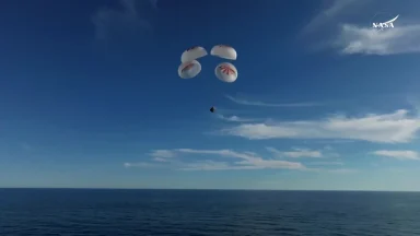 Space capsule descending with parachutes over ocean.