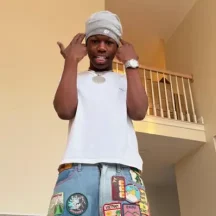 Man posing indoors wearing patchwork jeans and beanie