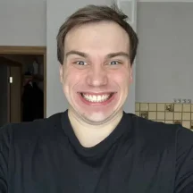 Man smiling widely indoors wearing black shirt