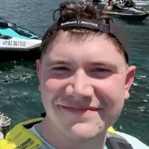 Person smiling near jet skis on a sunny lake