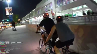 Two people ride tandem bike at night in city