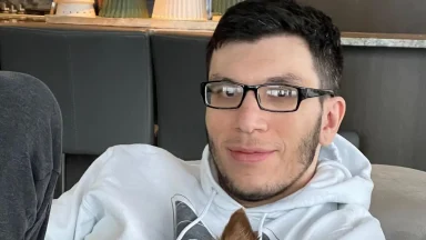 Person with glasses in a white hoodie indoors.