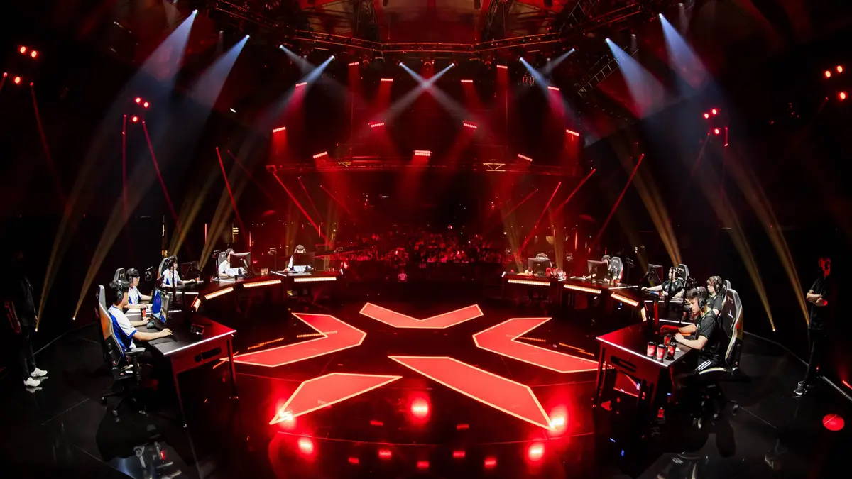 Esports teams compete on a red-lit arena stage.