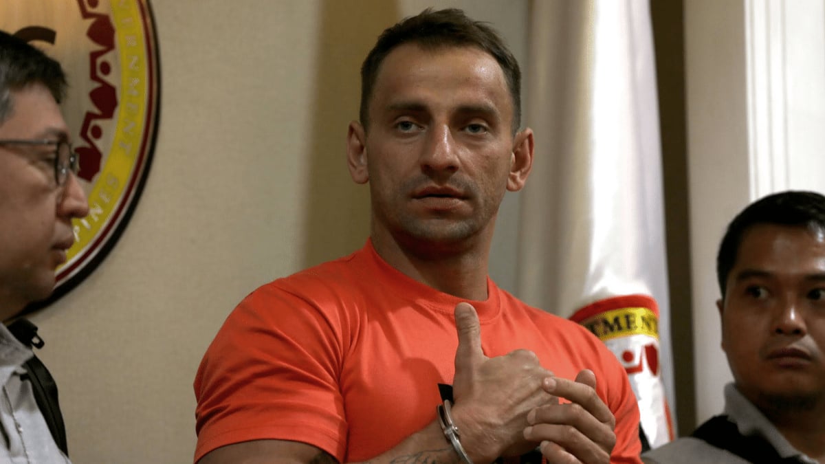 Handcuffed man in orange shirt seated indoors
